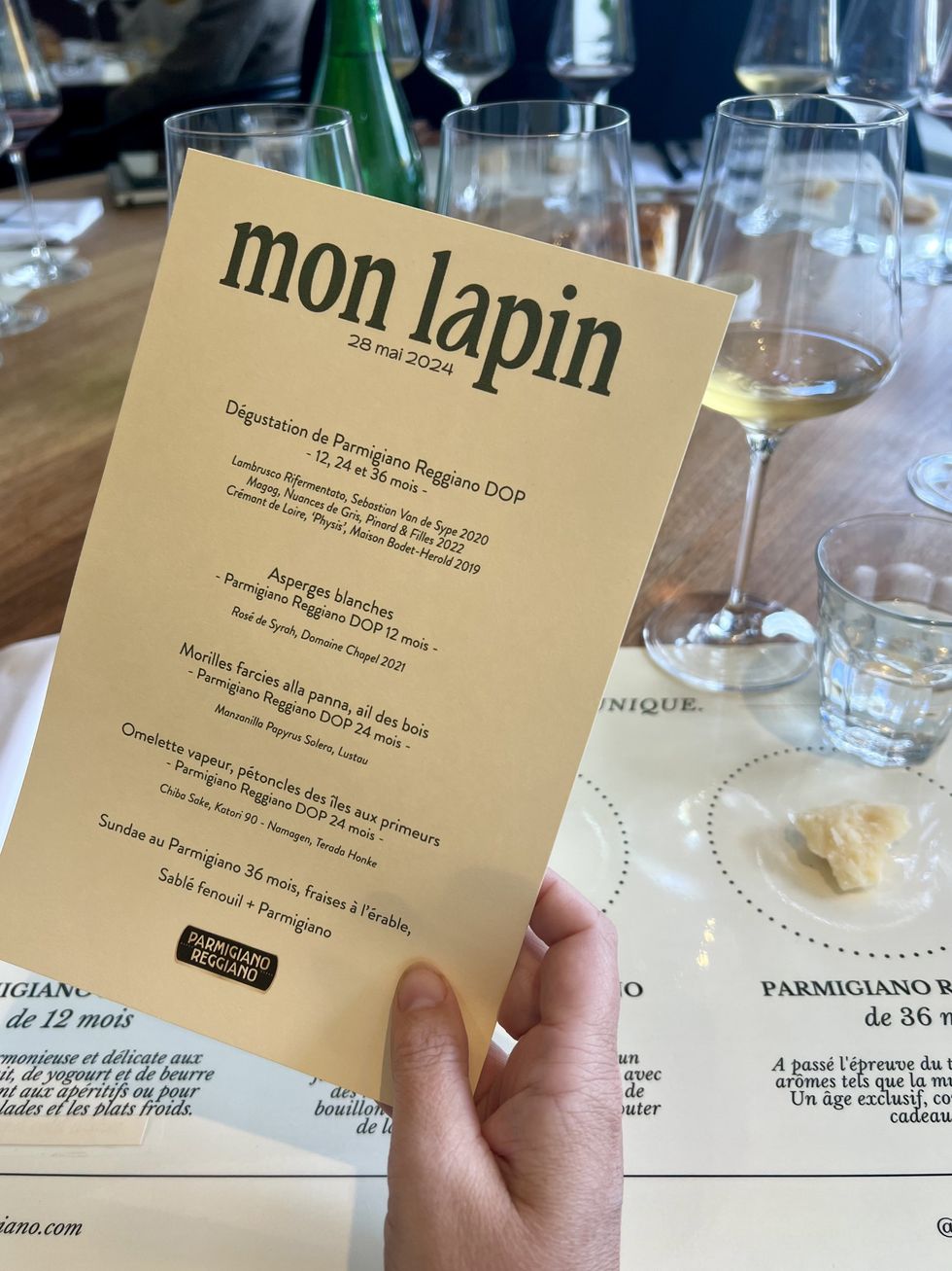 Une main tient un menu devant un napperon et un verre de vin blanc.