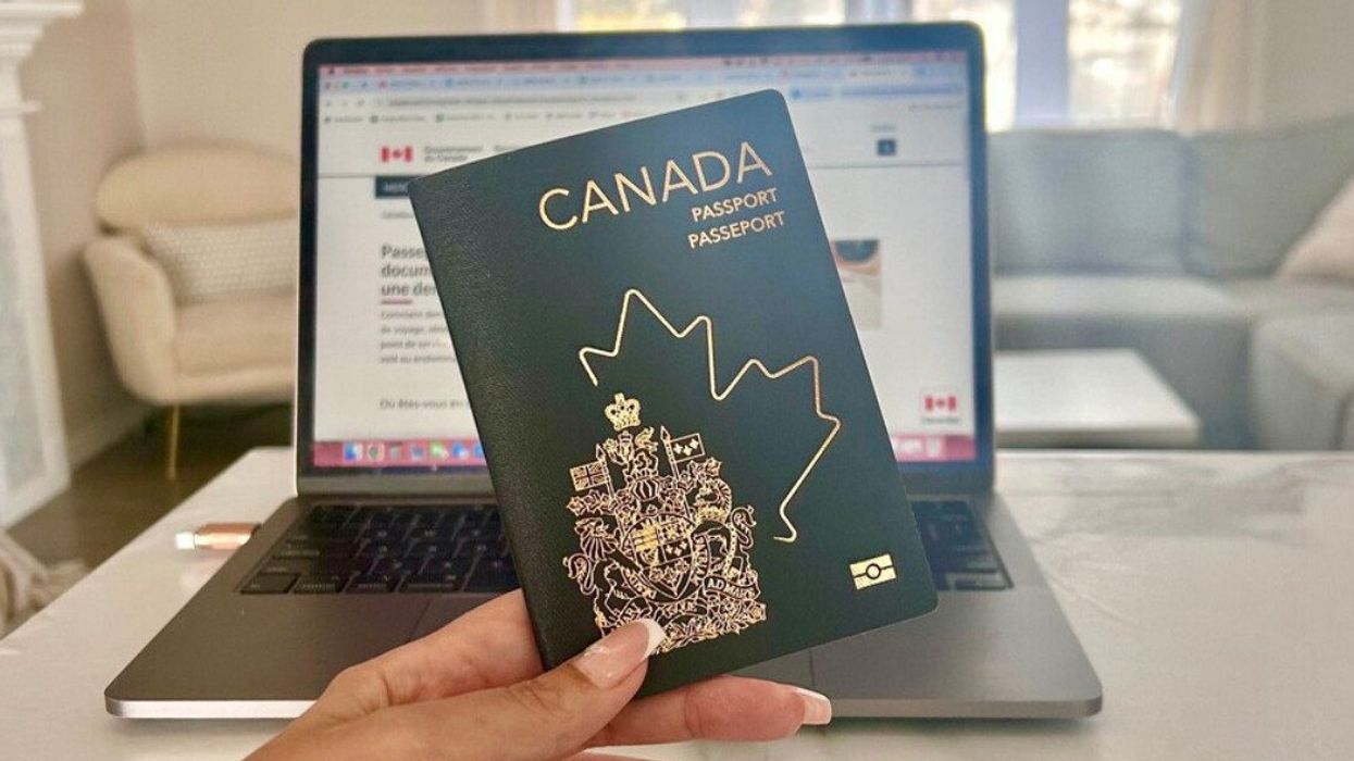 Une main tient un passeport canadien devant un ordinateur ouvert sur une page gouvernementale.