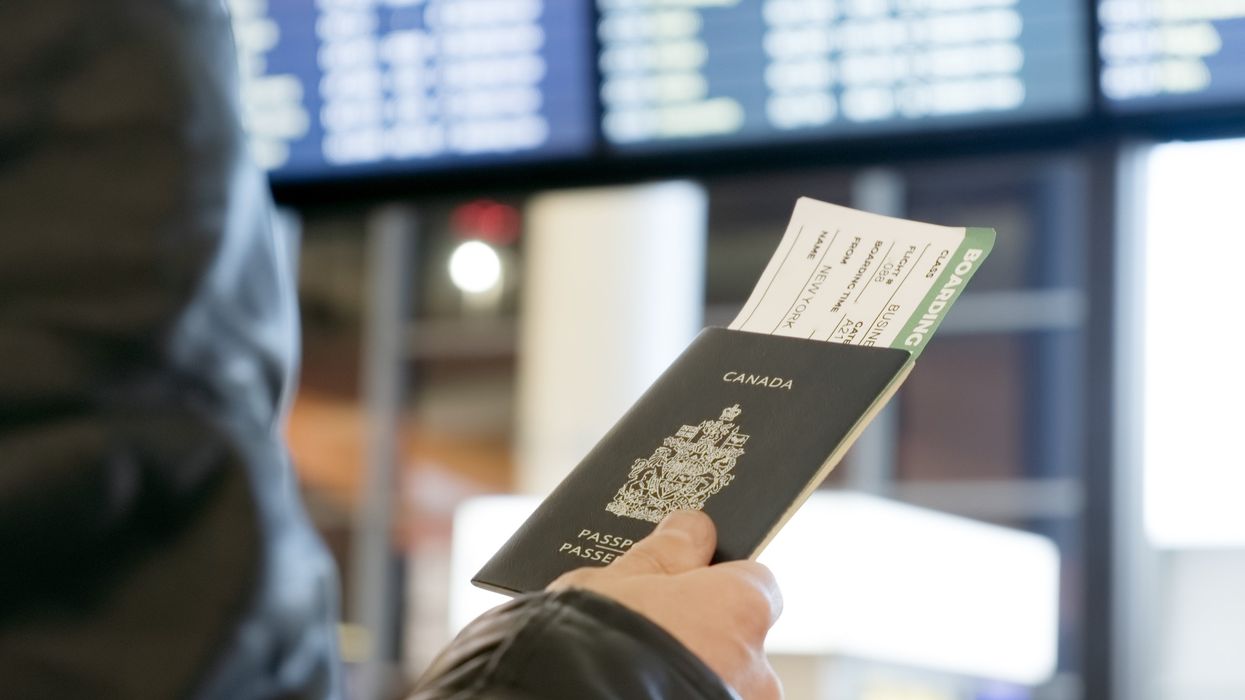 Une main tient un passeport canadien devant un tableau numérique dans un aéroport.
