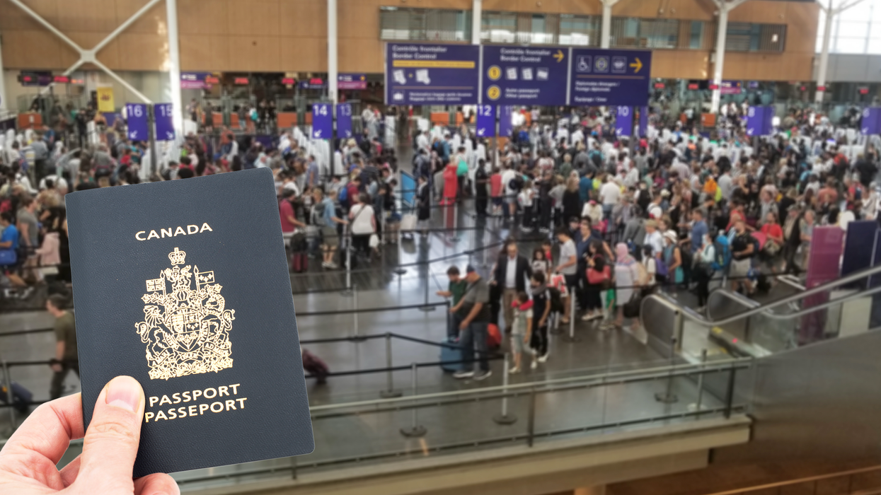 Une main tient un passeport devant l'aire des douanes de l'aéroport de Montréal.