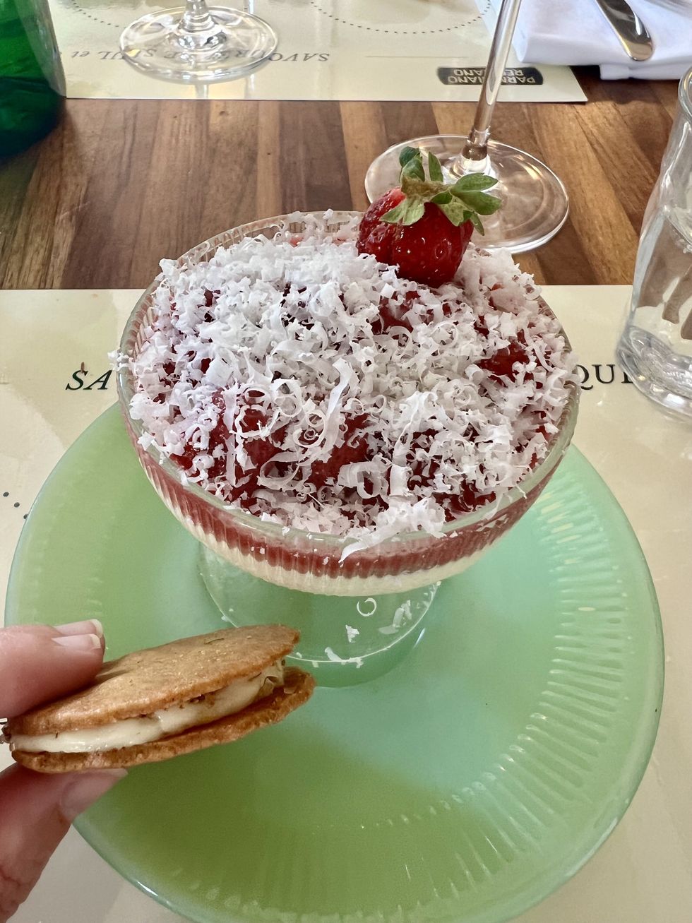 Une main tient un petit biscuit \u00e0 c\u00f4t\u00e9 d'un sundae \u00e0 la fraise plac\u00e9 sur une assiette verte.