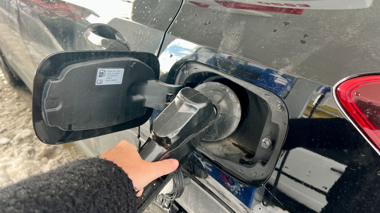 Une main tient un pistolet à essence devant son véhicule.