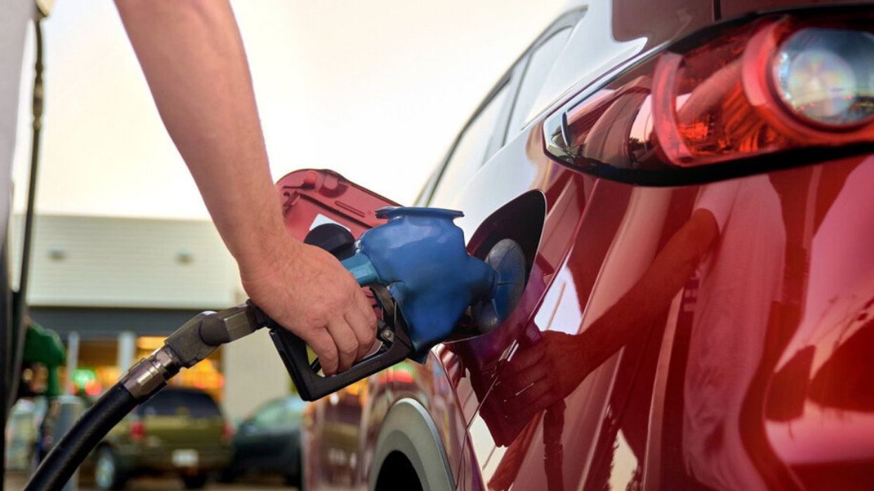 Une main tient un pistolet à essence pour remplir le réservoir de sa voiture rouge.