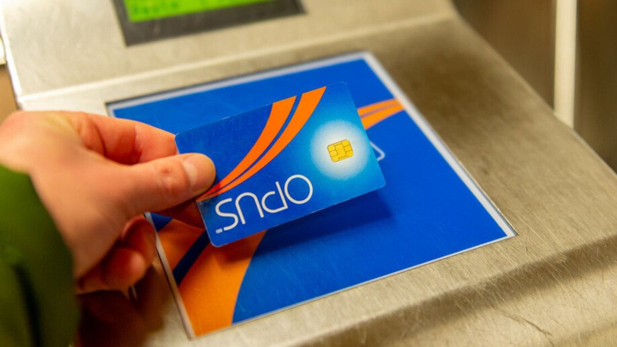 Une main tient une carte OPUS devant un lecteur installé dans une station de métro.