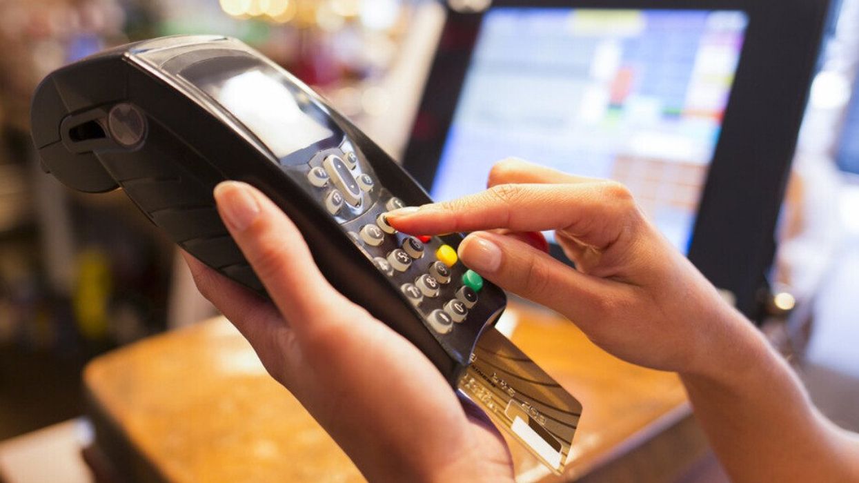 Une main tient une machine Interac et l'autre appuie sur les boutons du terminal de paiement.