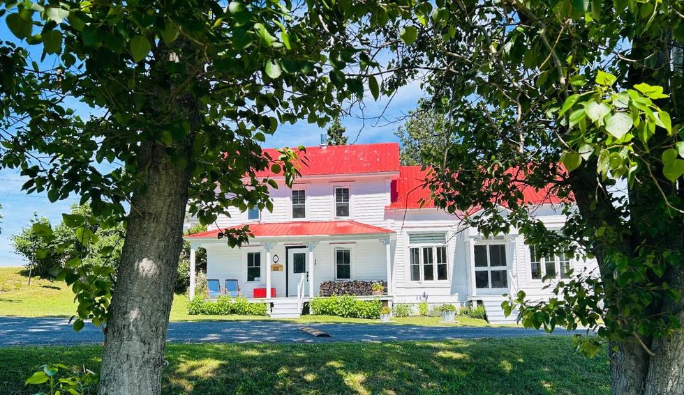 Une maison blanche avec un toit rouge entour\u00e9e d'arbre.