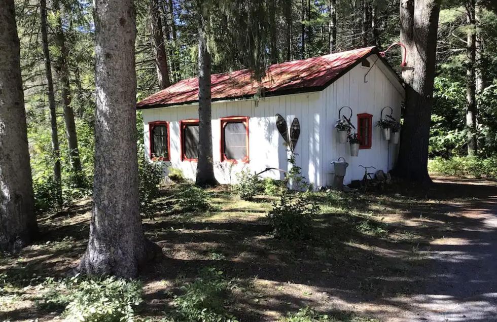 Une maisonnette blanche avec un toit bourgogne dans les bois.