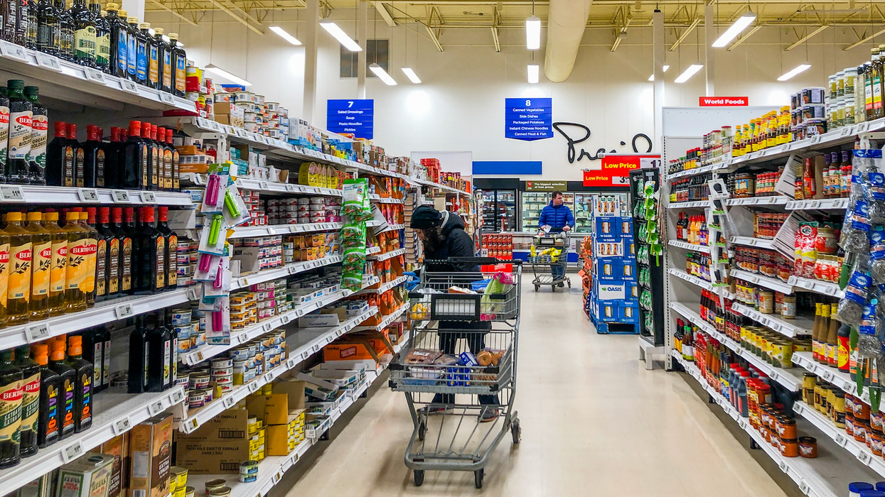 Une personne circule avec son panier et regarde des produits dans une allée d'épicerie.