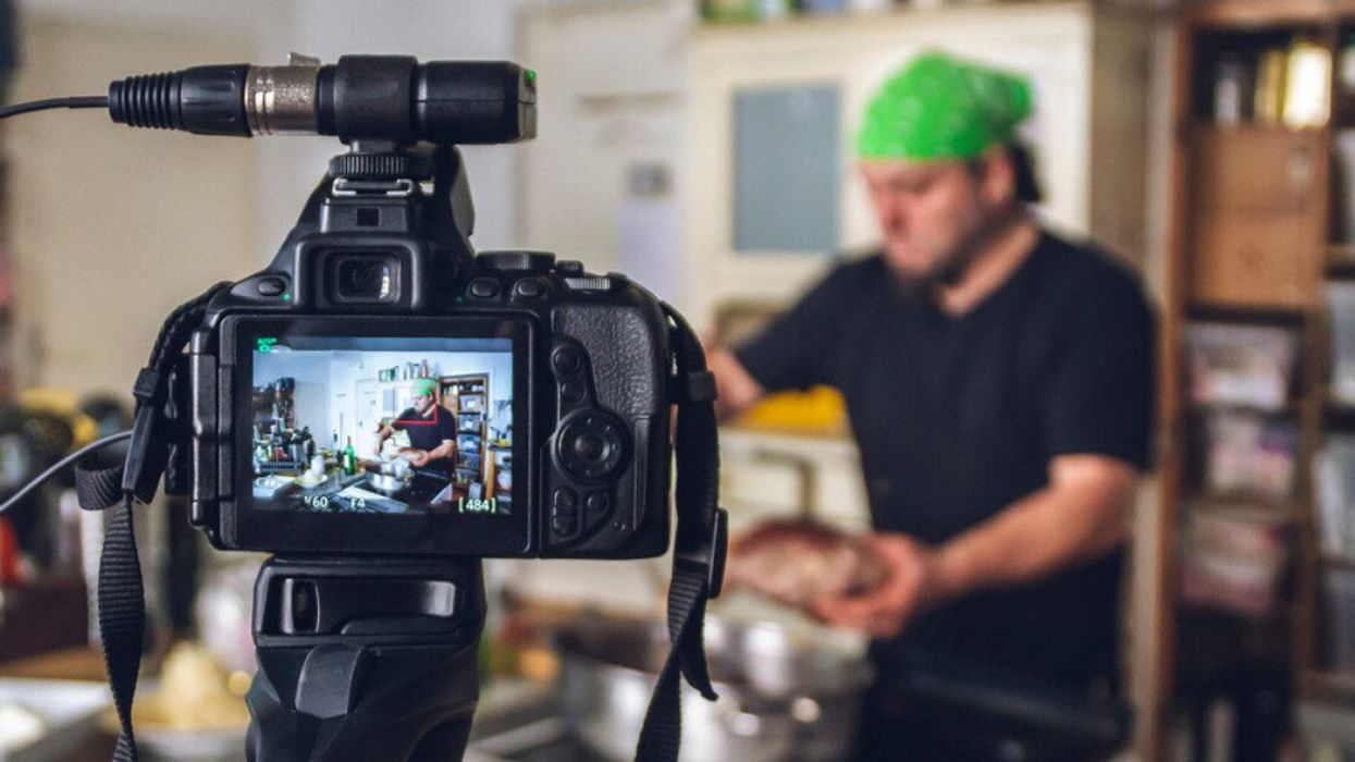 Une personne cuisine en arrière-plan pendant qu'une caméra enregistre en premier plan.