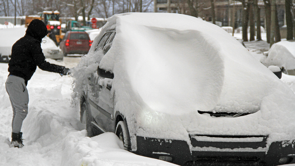 Une personne déblaie son véhicule recouvert de neige dans une rue à Montréal.
