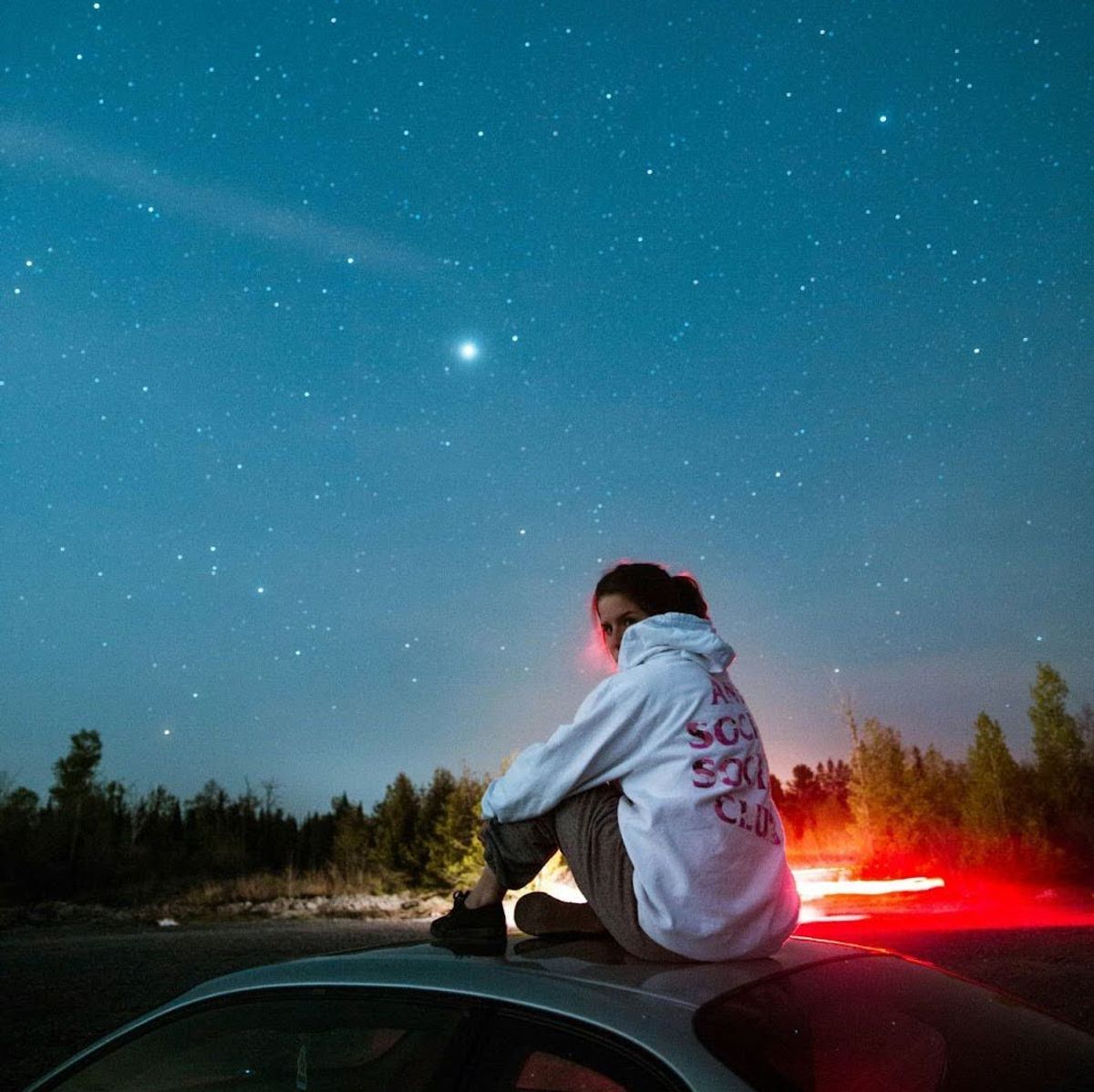 Une personne est assise sur le toit d'une voiture sous un ciel.