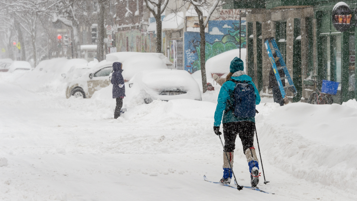 Une personne fait du ski et une autre est debout devant un véhicule dans une rue enneigée à Montréal.