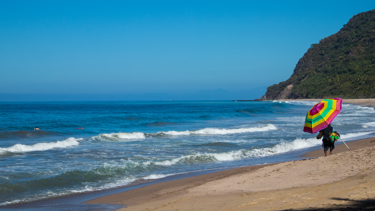 Une personne marche avec un gros parasol sur le bord d'une plage.