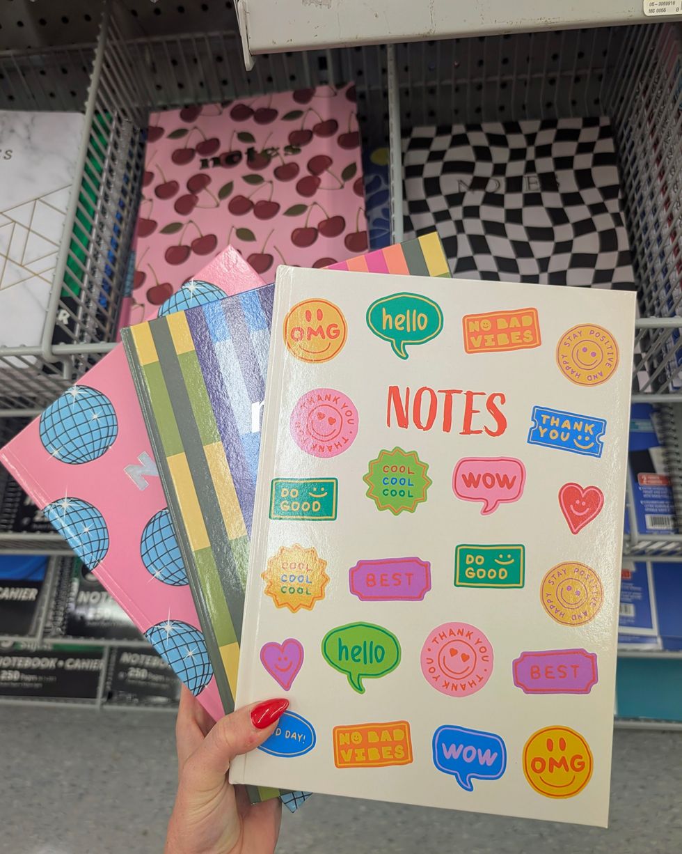 Une personne qui tient trois cahiers de notes \u00e0 motifs color\u00e9s dans la rang\u00e9e des fournitures scolaires chez Dollarama.