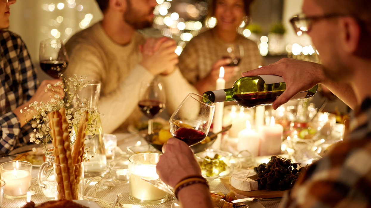 Une personne rempli une coupe de vin rouge lors d'un souper festif.