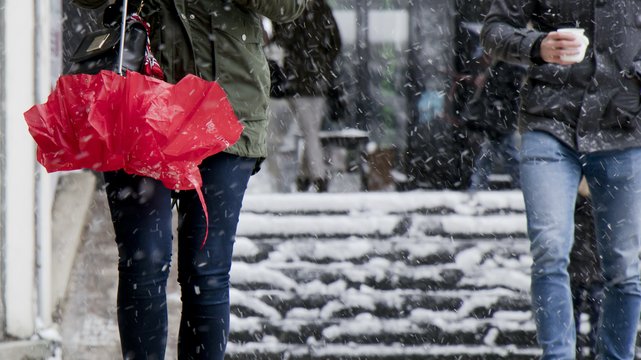 Une personne tient un parapluie rouge entre ses mains et une autre, un café sur une place publique enneigée.