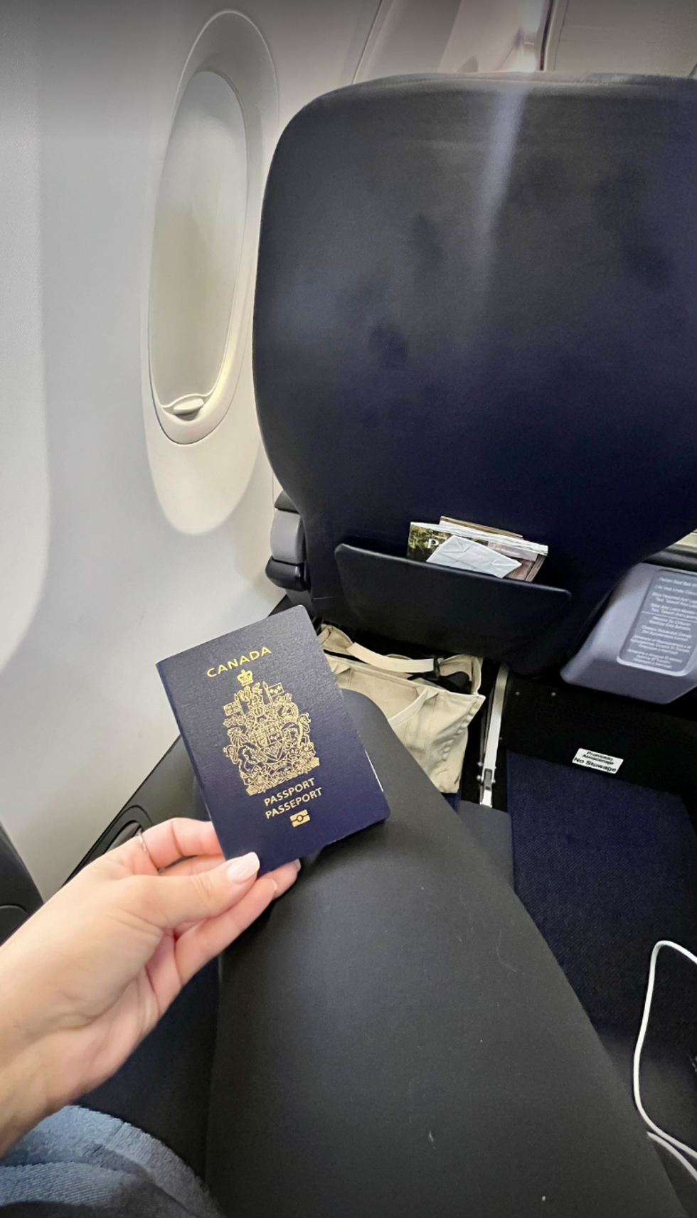 Une personne tient un passeport canadien, dans la classe affaires de l'avion.