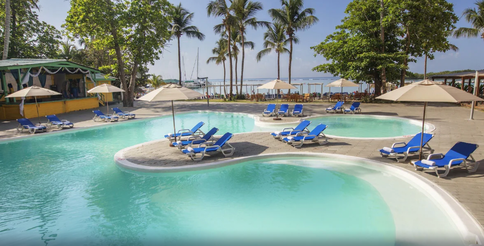 Une piscine d'h\u00f4tel avec des chaises longues en avant-plan de la mer et des palmiers.
