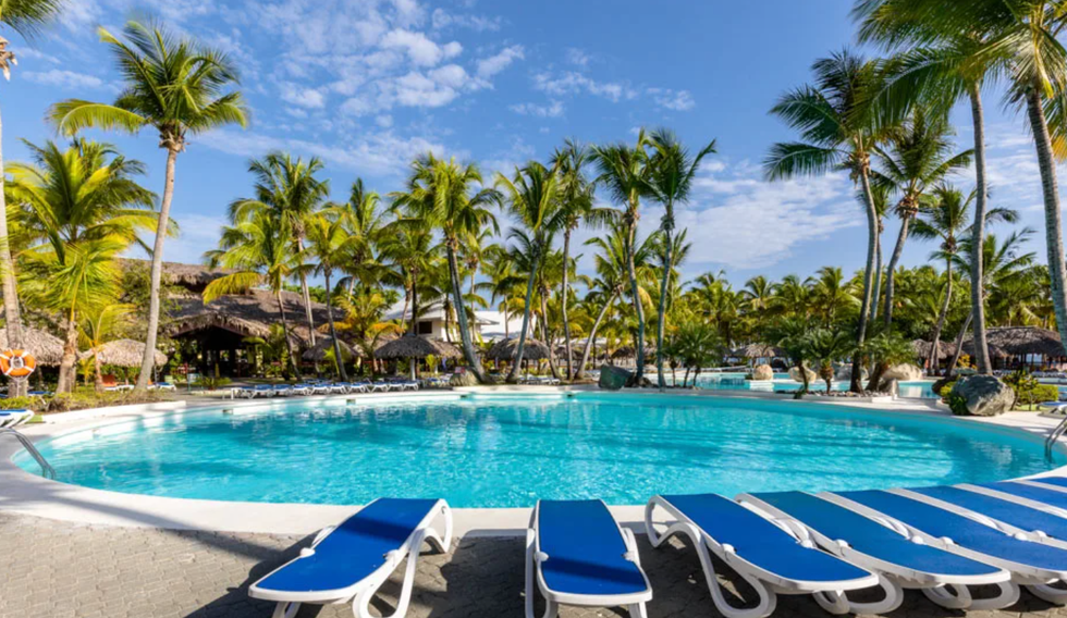 Une piscine entour\u00e9e de chaises longues bleues et de palmier \u00e0 l'h\u00f4tel Playabachata Spa Resort \u00e0 Puerto Plata.