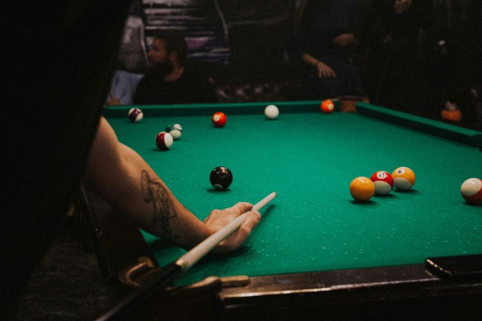 Une queue repose sur une table de billard dans un bar sombre.