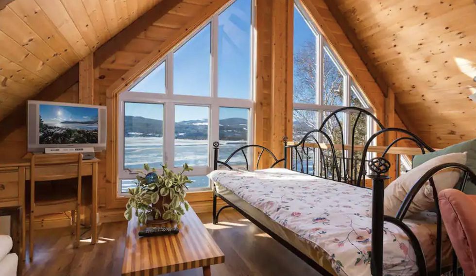 Une salle de s\u00e9jour en bois avec bureau, t\u00e9l\u00e9, table de salon, futon et de grandes baies vitr\u00e9es.