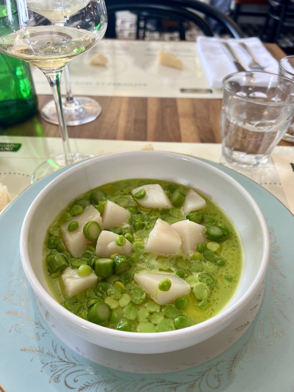Une soupe verte dans un bol avec des petits pois verts, asperges en rondelles et p\u00e9toncles.