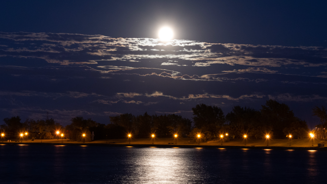 Une super lune dans un ciel nuageux et qui se reflète sur l'eau d'un lac.