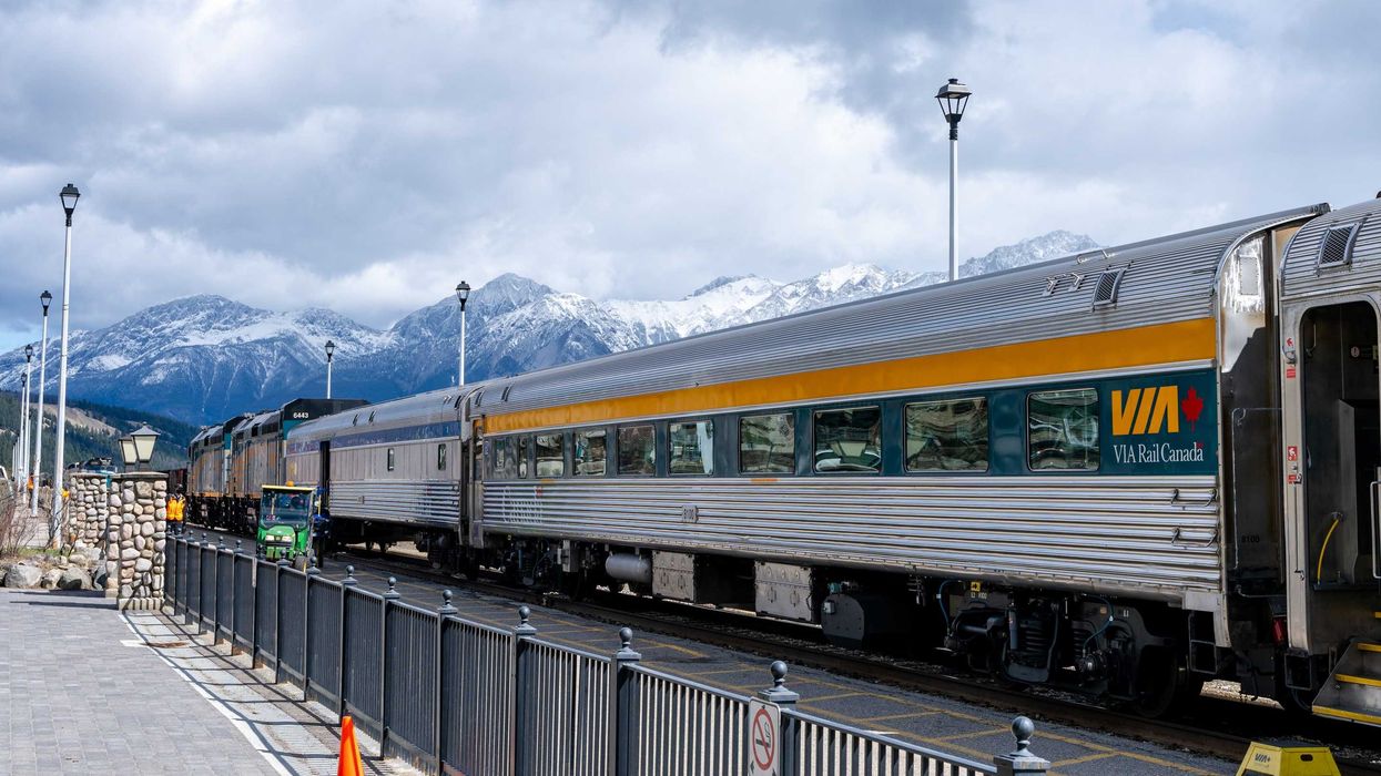 via rail train on the tracks in jasper, alberta with mountains in the background