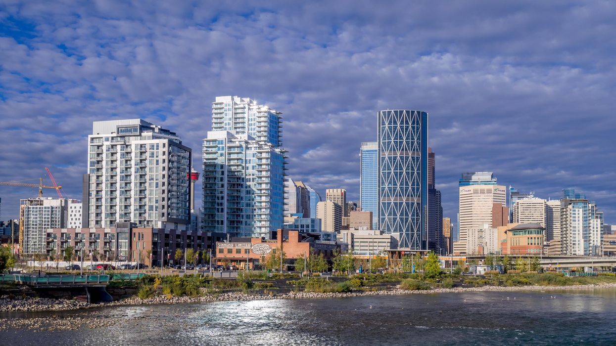 View of condo buildings in Calgary's East Village behind a body of water.