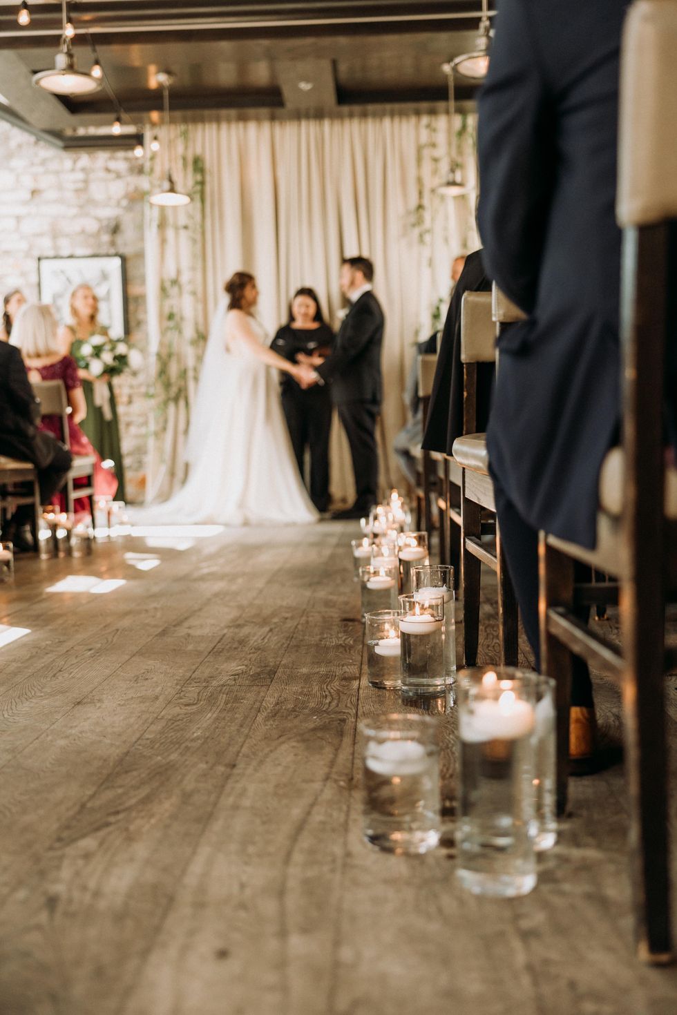 View of the wedding aisle lined with candles and a couple at the front with the officiant.