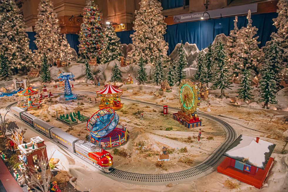 Village de No\u00ebl avec des man\u00e8ges, un train et des sapins.