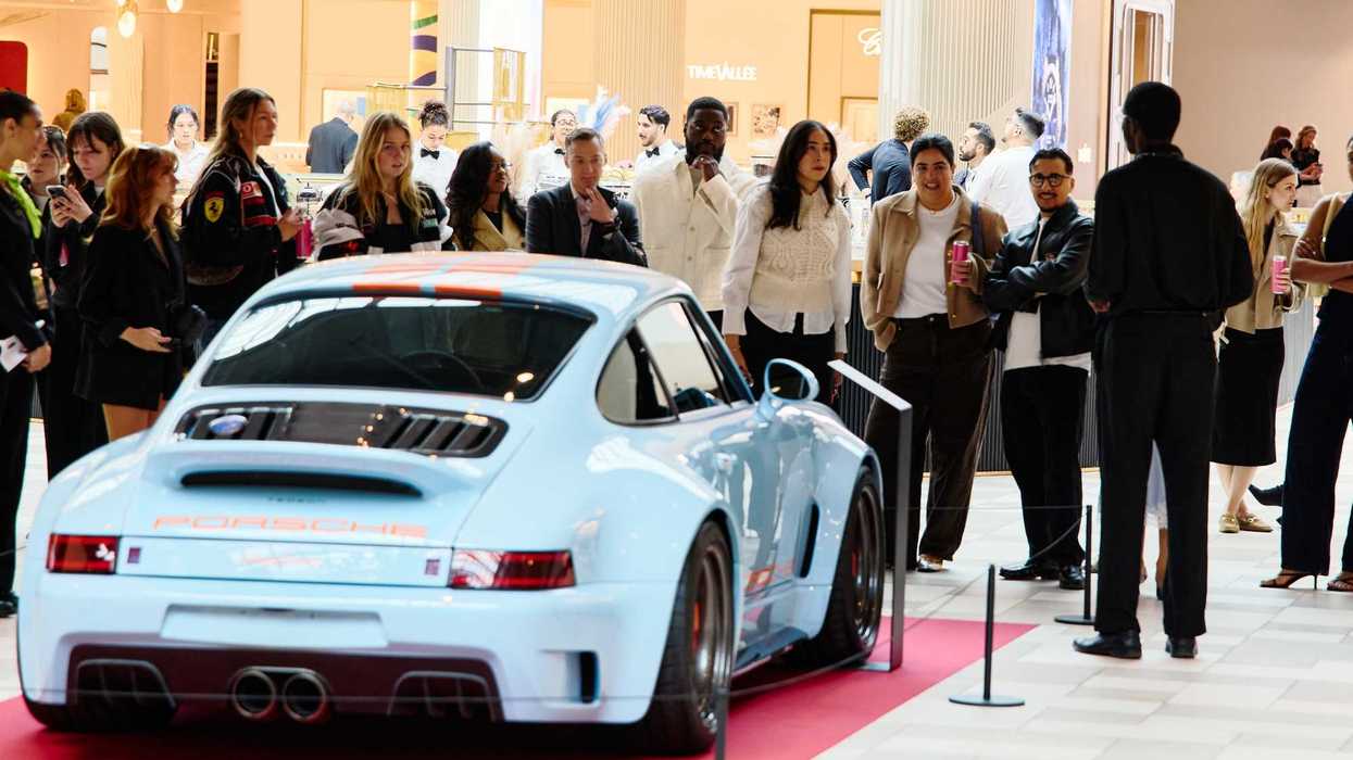 Voiture Porsche bleue exposée sur tapis rouge à l’intérieur du centre commercial Royalmount avec visiteurs autour.