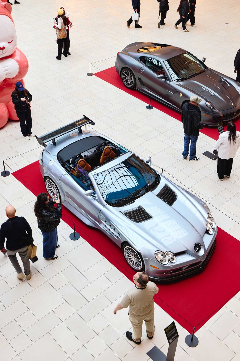 =Voitures Mercedes-Benz et Ferrari expos\u00e9es sur tapis rouges \u00e0 l\u2019int\u00e9rieur du centre commercial Royalmount avec visiteurs autour.