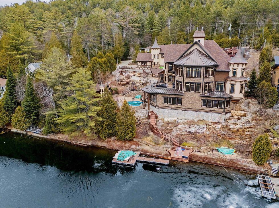 Vue a\u00e9rienne d\u2019une grande maison de style ch\u00e2teau en pierre et bois, construite en bordure du lac Rouge, avec quai priv\u00e9 et terrain bois\u00e9.