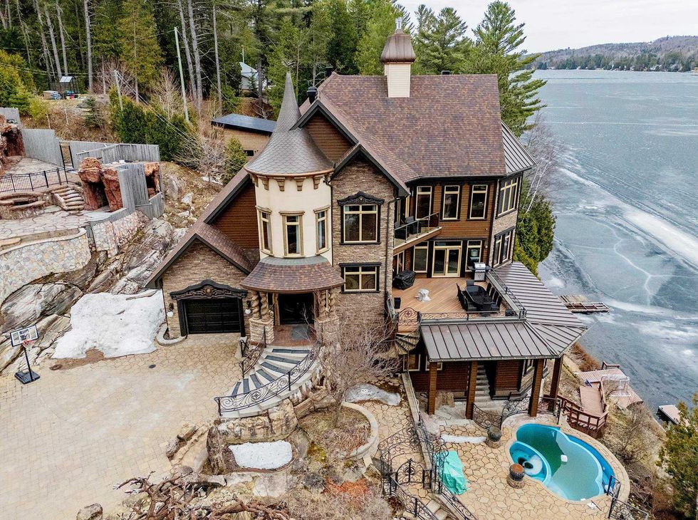 Vue a\u00e9rienne d\u2019une grande maison de style ch\u00e2teau en pierre et bois situ\u00e9e au bord du lac Rouge, avec quai priv\u00e9 et spa ext\u00e9rieur.