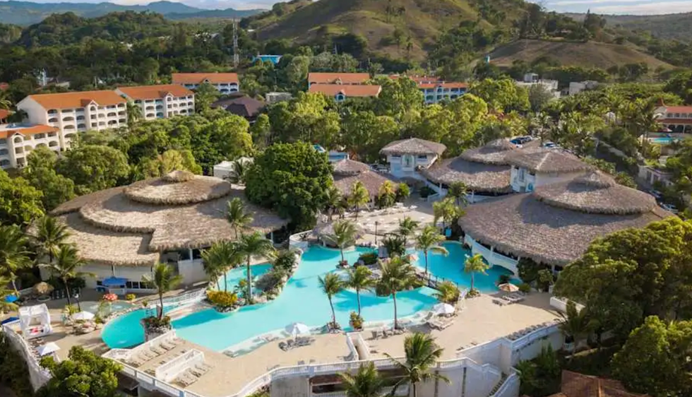 Vue a\u00e9rienne du Cofresi Palm Beach Resort and Spa entour\u00e9 de palmiers et d\u2019une grande piscine turquoise.