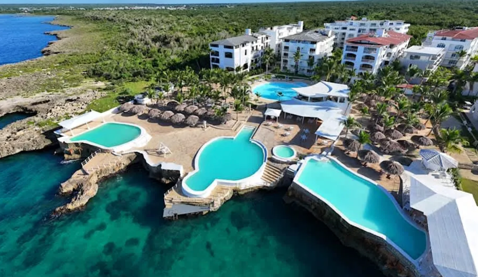 Vue a\u00e9rienne du complexe install\u00e9 au bord d\u2019une mer turquoise, avec plusieurs piscines de formes uniques construites sur les rochers.