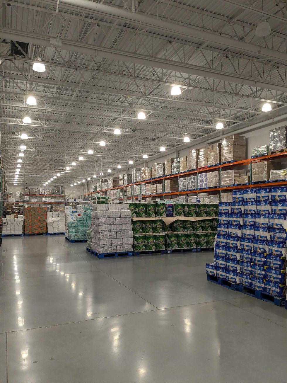 Warehouse aisle with stacked pallets of boxed products under bright overhead lights