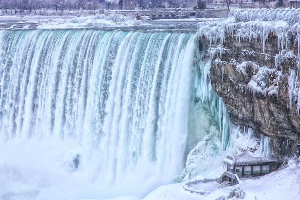 Water cascades over the Horseshoe Falls in Niagara Parks next to a frozen-over lookout.