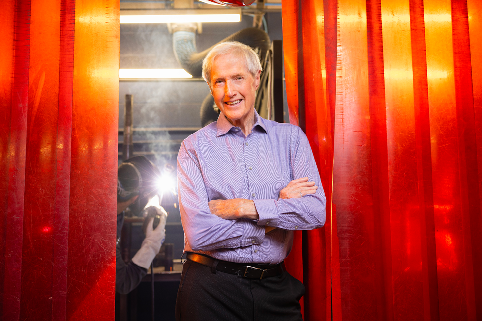 Weldtech founder Jim Murphy smiles at the camera with his arms crossed as a student welds in the background. 