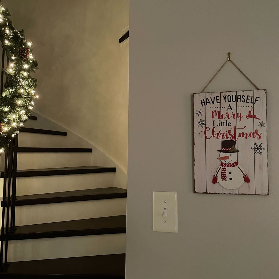 white have yourself a merry little christmas hanging sign with a snowman and snowflakes on a wall beside a staircase with garland on the handrail