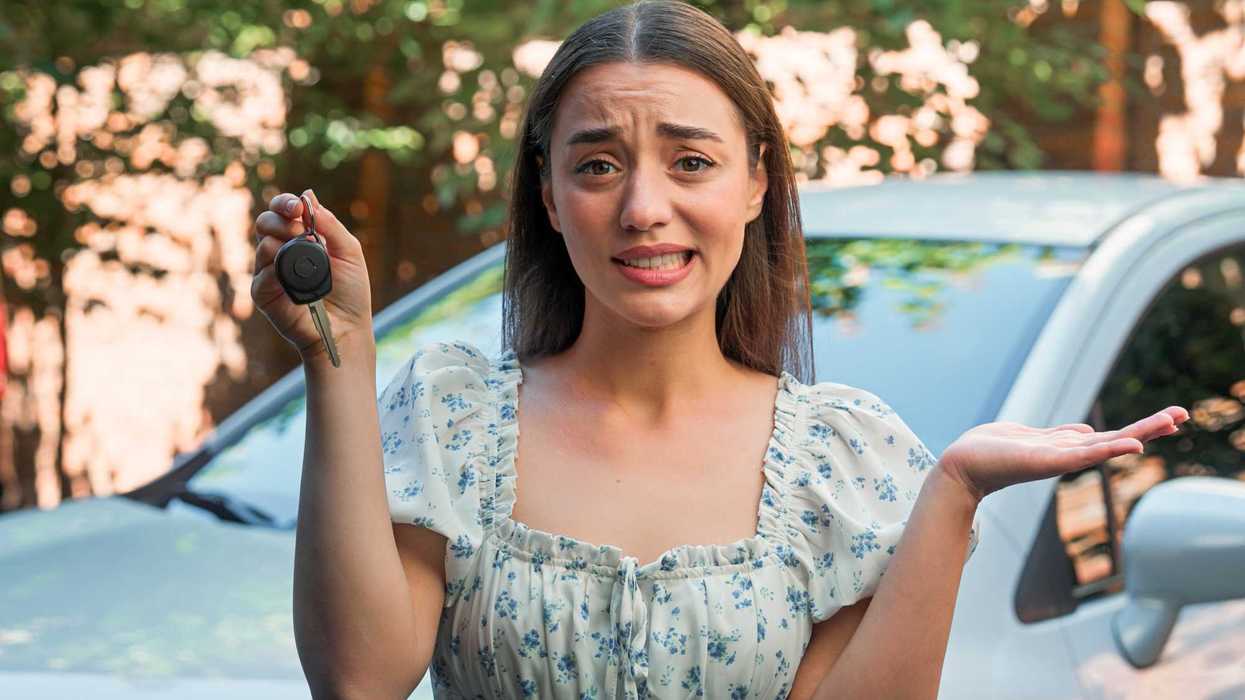Woman holding car keys shrugs uncertainly in front of a car.
