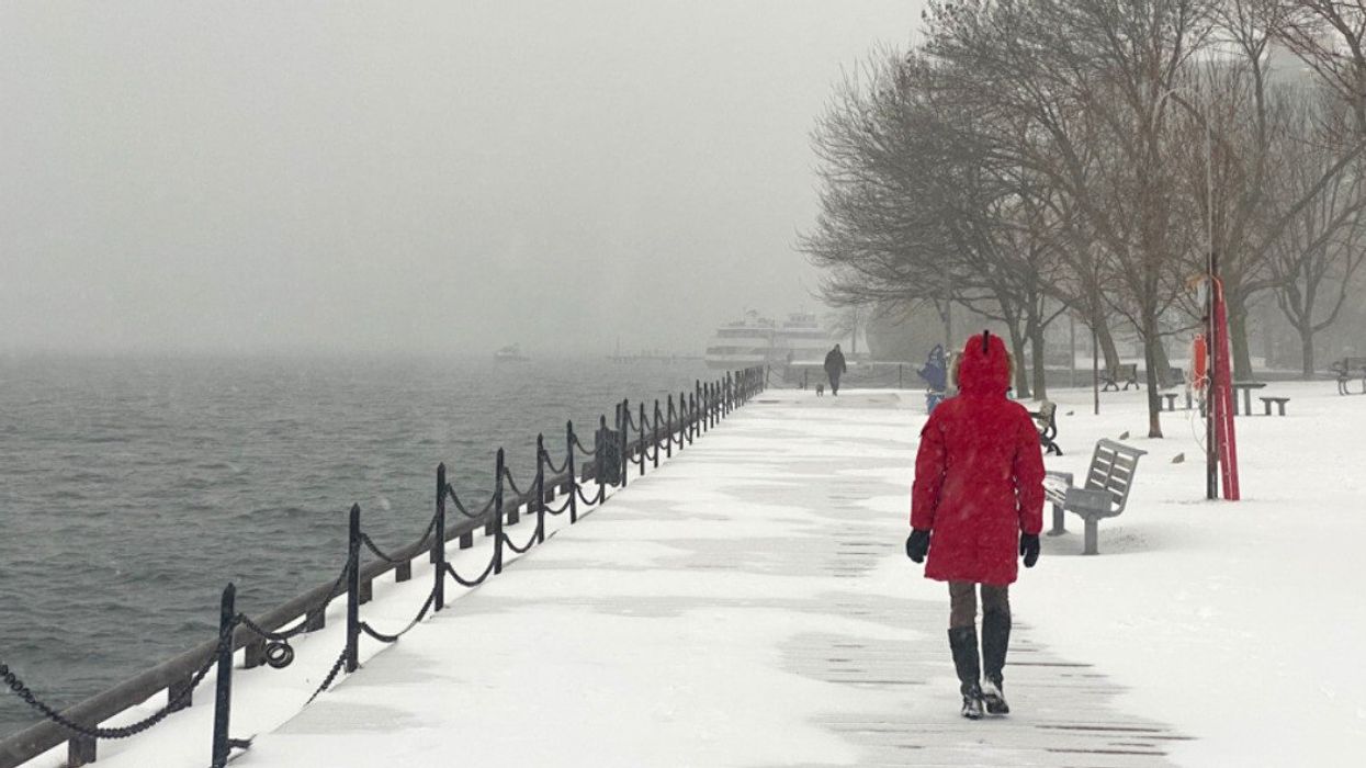 Woman in red winter coat walking on a wooden deck covered in snow.