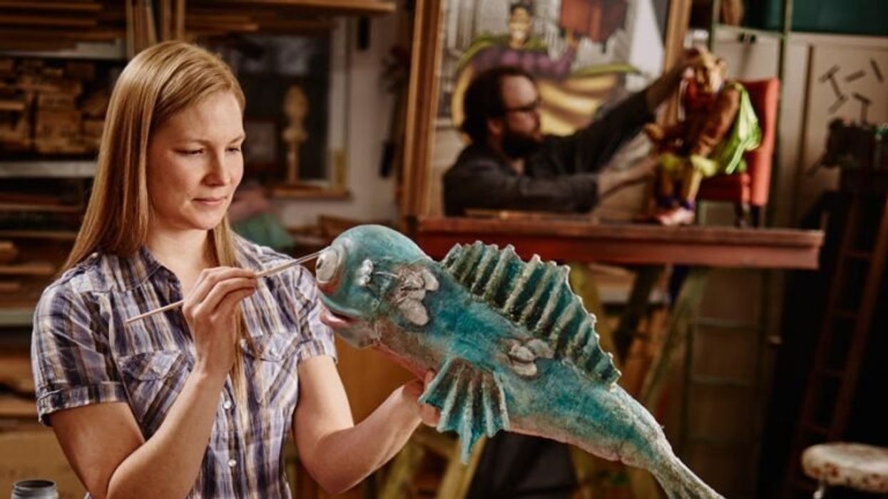 Woman painting a fish puppet.
