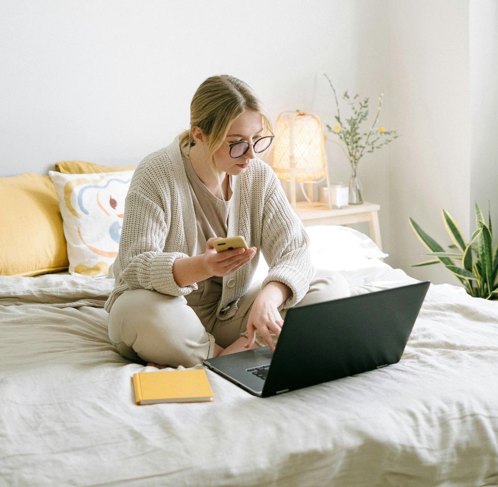 Woman sitting on bed while using a laptop.