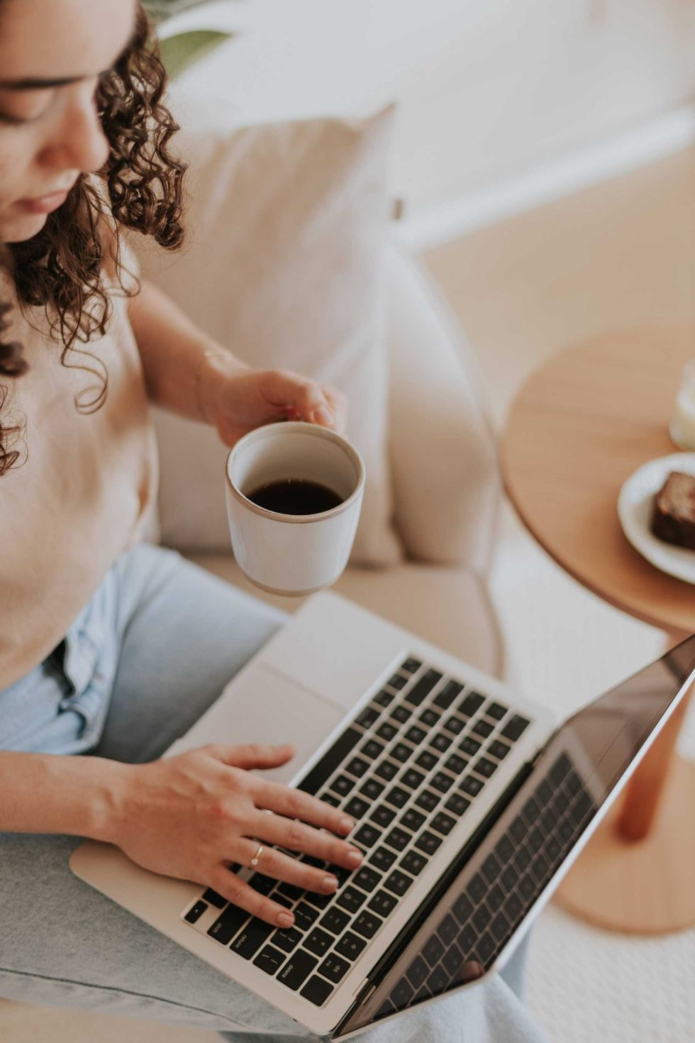Woman using a laptop while holding a cup of coffee at home.