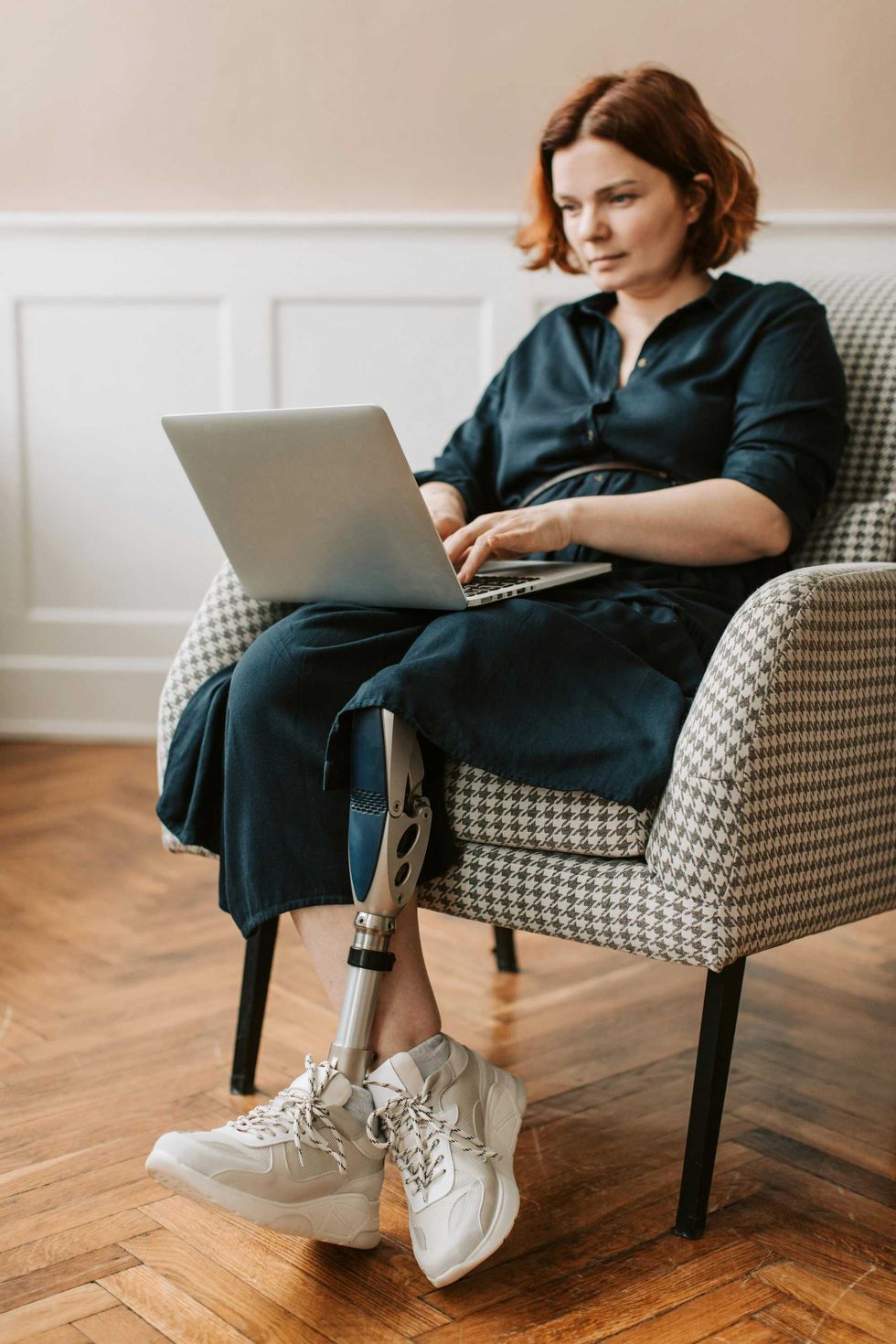 Woman with a prosthetic leg using a laptop at home, representing accessibility, resilience, and everyday independence.