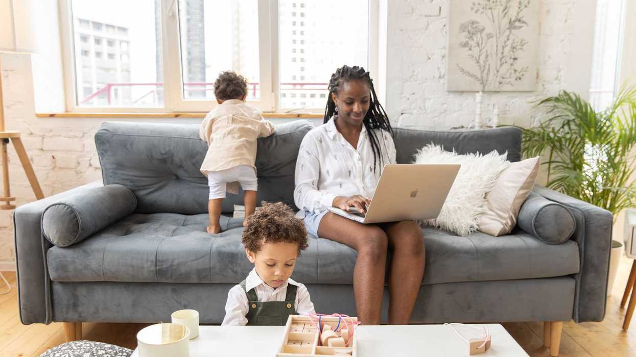 Woman working on a laptop at home with two young children.