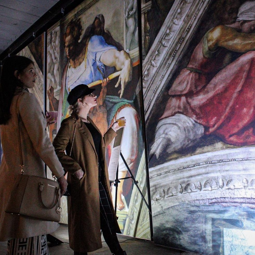Women admiring ceiling frescos from Michelangelo's Sistine Chapel painting.