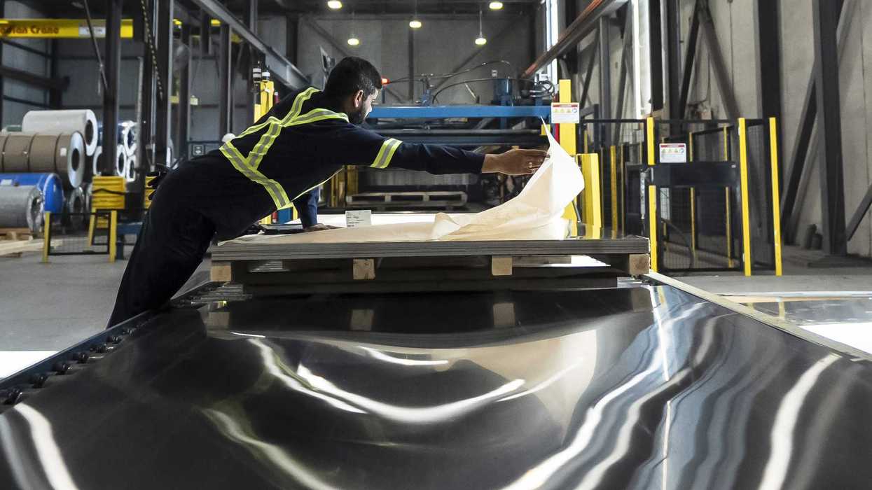 Workers inspect sheets of steel at a factory.